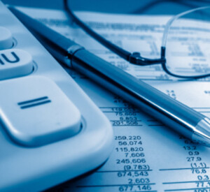 close up of a calculator, spreadsheets, a pair of glasses and a pen to signify pricing