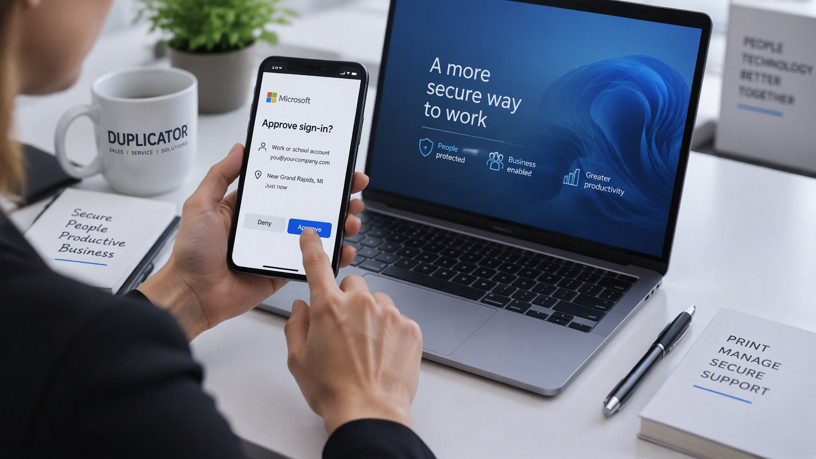 Office employee approving a multi-factor authentication sign-in prompt on a smartphone next to a laptop.